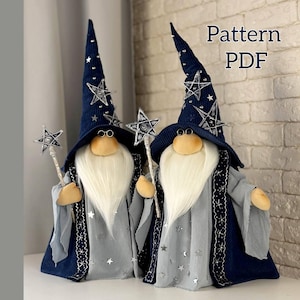 Pode incluir: Duas bonecas de pelúcia com tema de mago. Cada boneca tem uma longa barba branca, óculos redondos e um chapéu azul alto adornado com estrelas prateadas. Elas usam vestes cinzentas com acabamentos prateados e seguram varinhas em forma de estrela. O texto "Pattern PDF" é visível.