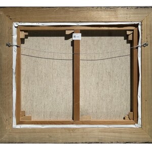May include: The back of a framed canvas painting. The wooden frame is a light brown color with a dark brown trim. The canvas is stretched over a wooden frame with a wire for hanging.
