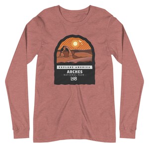 May include: A heather red long-sleeve t-shirt with a graphic of Arches National Park in Utah. The graphic features a sunset, a rock formation, and the text "Explore America Arches National Park L48".