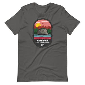 May include: Dark gray t-shirt featuring a graphic of a landscape with a rock formation, sunset, and text that reads "Explore Kentucky Jump Rock - Red River Gorge - 148". The shirt is made of a soft material.