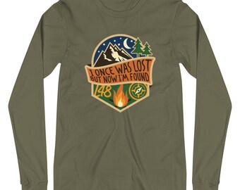 Op de afbeelding: Een groen longsleeve t-shirt met een afbeelding van een bergketen, een kampvuur en een kompas. De tekst op de afbeelding luidt "I once was lost but now I'm found 148".