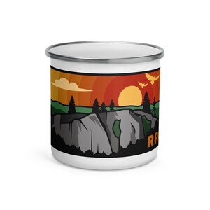 May include: White enamel mug with a colorful illustration of a sunset over a mountain range. The illustration features a red, orange, and yellow sunset with a gray mountain range and green trees. The text "Red Rock Canyon" is printed on the mug.