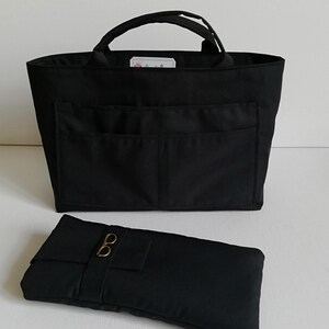 Peut inclure: Un sac fourre-tout en tissu noir avec deux poignées supérieures et deux poches extérieures à l'avant, accompagné d'une pochette rectangulaire en tissu noir assortie avec une petite breloque en métal en forme de lunettes.