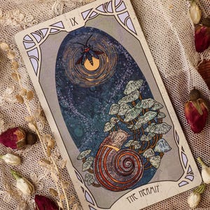 May include: A tarot card illustration depicting a snail with a mushroom-covered shell. Above, a moth flies near a glowing orb. The card is framed with decorative borders and the words "THE HERMIT".
