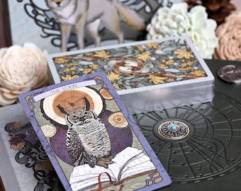 May include: A tarot card titled The Scribe featuring an owl perched on an open book, resting on a dark green textured surface next to a deck of cards with a botanical back design. The card has a purple border and a circular wood grain background.