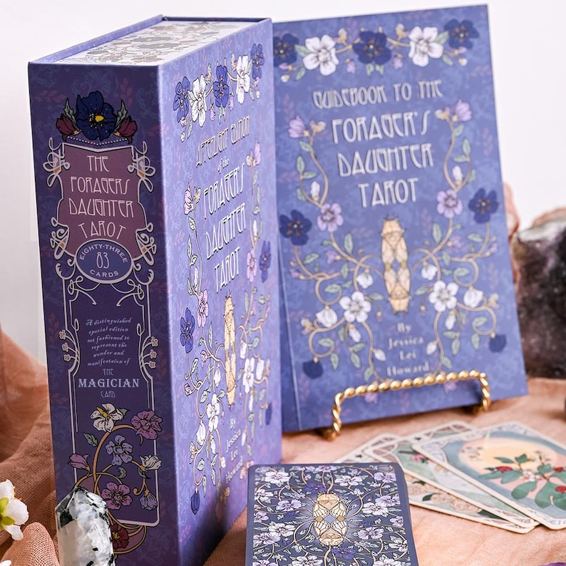 May include: A tarot card set with a purple box and guidebook. The box and guidebook feature floral designs and the text "The Gorda's Daughter Tarot." The set includes 83 cards, with the Magician card visible.