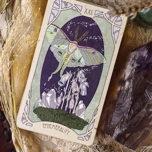 May include: A tarot card depicting a Luna moth with green and purple hues, set against a dark purple, starry backdrop. The card has a pale green border and the word "EPHEMERALITY" at the base.