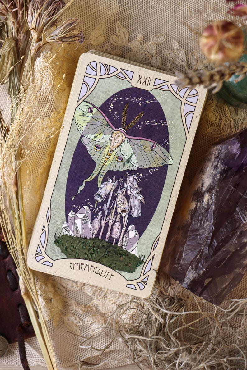 May include: A tarot card depicting a Luna moth with green and purple hues, set against a dark purple, starry backdrop. The card has a pale green border and the word "EPHEMERALITY" at the base.