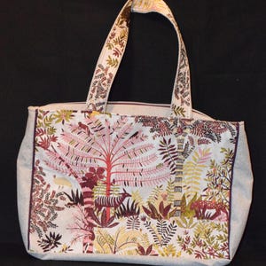Peut inclure: Un sac cabas blanc avec un motif floral rose, vert et marron. Le sac a deux longues anses et une fermeture éclair.