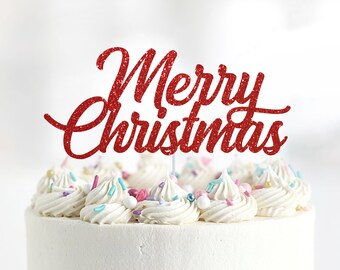 May include: Red glitter cake topper with the words "Merry Christmas" on a white frosted cake with colorful sprinkles.