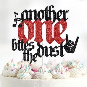 May include: A red glitter cake topper with black text that reads "Another One Bites The Dust" with a rock and roll hand gesture.