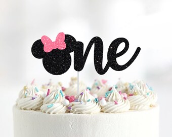 May include: Black glitter cake topper with the word "one" and a pink glitter bow on a black silhouette of Mickey Mouse's head.