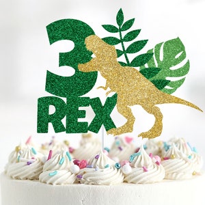 May include: Green glitter cake topper with a gold glitter dinosaur silhouette, the number 3, and the word "REX".