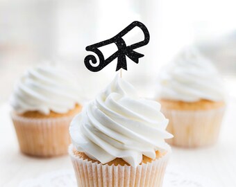 May include: Three white cupcakes with white frosting. The cupcake in the center has a black glitter graduation cap topper.