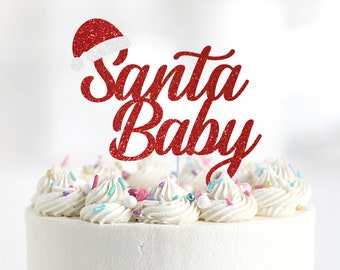 May include: Red glitter cake topper with the words "Santa Baby" and a red glitter Santa hat. The topper is on top of a white frosted cake with sprinkles.