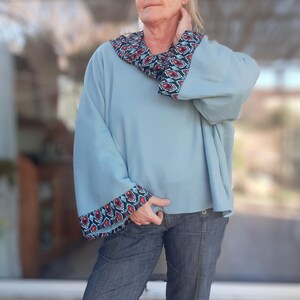 Peut inclure: Un pull surdimensionné bleu clair avec une bordure à motifs colorés autour de l'encolure et des poignets. Le pull est fait d'un matériau doux et confortable.