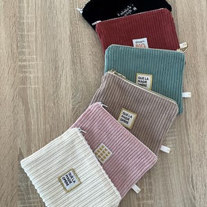 Op de afbeelding: Zes verschillende ritszakjes van corduroy stof in verschillende kleuren. De zakjes hebben verschillende zinnen erop gedrukt, waaronder "I make a wish", "dream big", "que la magie opere" en "que la magie opere".