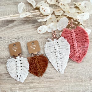 Op de afbeelding: Drie handgemaakte macramé veren sleutelhangers in wit, bruin en roze. Elke sleutelhanger heeft een klein label met de tekst "Handmade with love".