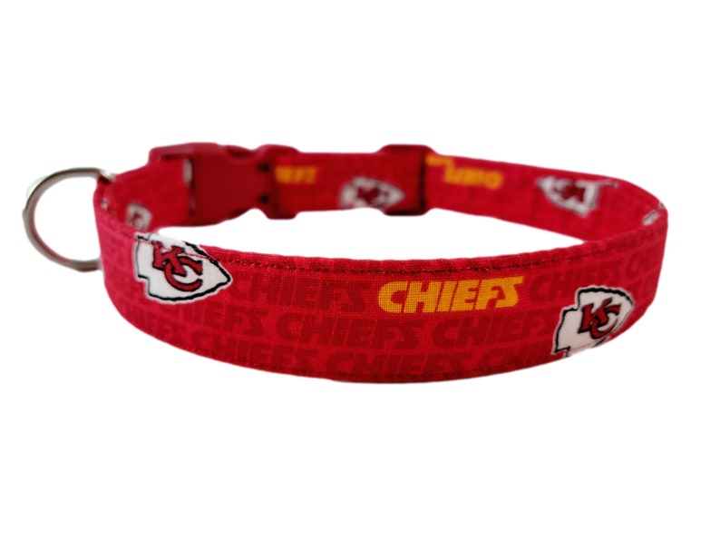 May include: Red dog collar featuring a white and yellow Kansas City Chiefs logo and the word "CHIEFS" repeated on the collar.