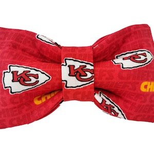 Pode incluir: Gravata borboleta vermelha com um padrão de logotipo do Kansas City Chiefs branco e amarelo. A gravata borboleta é feita de tecido e tem uma forma clássica de gravata borboleta.