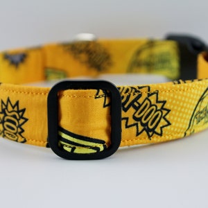 May include: Yellow dog collar with a black buckle. The collar features a repeating pattern of cartoon graphics and text in black. The text includes the word "YIP-DOO" in a speech bubble.