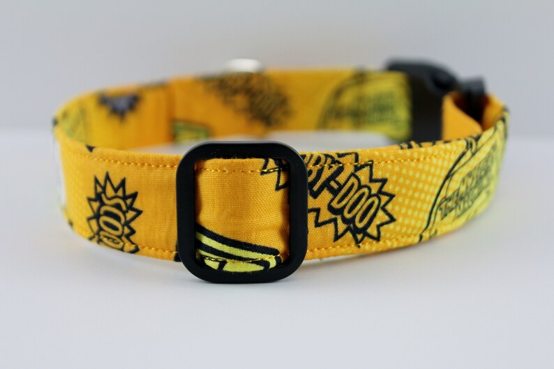 May include: Yellow dog collar with a black buckle. The collar features a repeating pattern of cartoon graphics and text in black. The text includes the word "YIP-DOO" in a speech bubble.