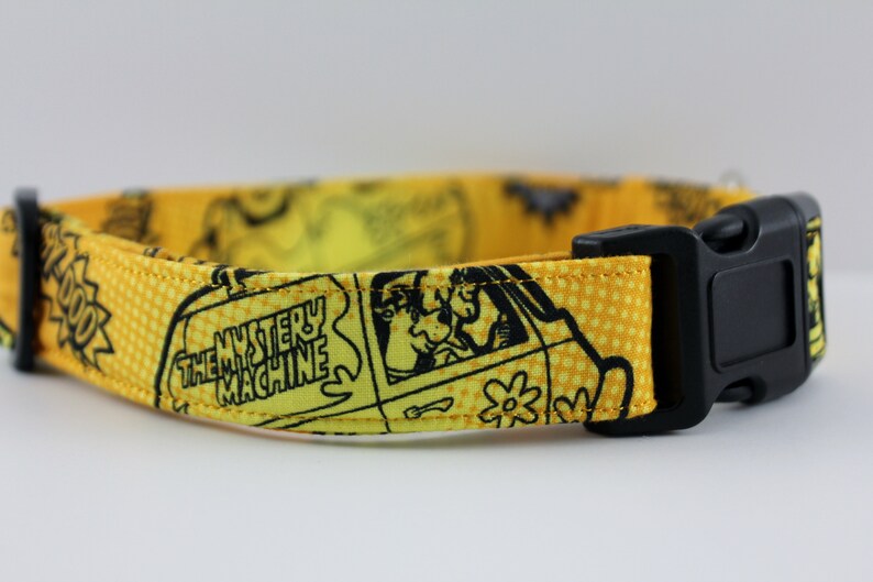 May include: Yellow dog collar featuring a black and white cartoon design with the text "THE MYSTERY MACHINE". The collar has a black plastic buckle and a matching adjustable strap.