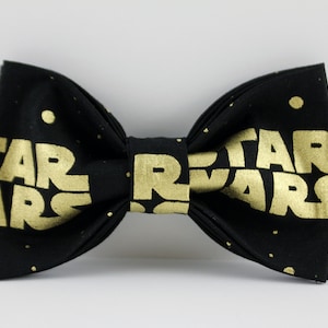 May include: A black bow tie with the words "STAR WARS" in gold lettering. The bow tie has a repeating pattern of small gold dots. The bow tie is a formal accessory.