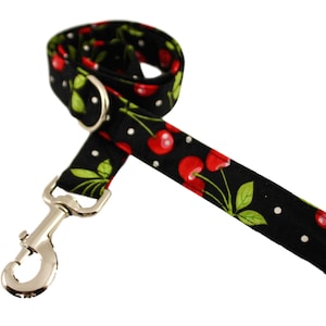 May include: Black and white dog leash with a red cherry print. The leash has a silver clip.
