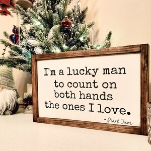 May include: A wooden sign with a white background and black text. The text reads "I'm a lucky man to count on both hands the ones I love. - Pearl Jam".