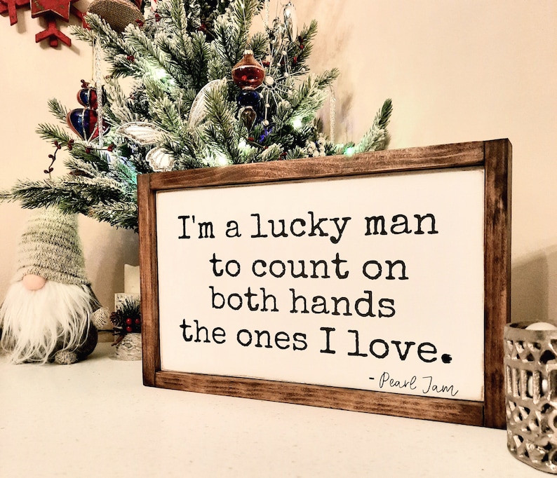 May include: A wooden sign with a white background and black text. The text reads "I'm a lucky man to count on both hands the ones I love. - Pearl Jam".