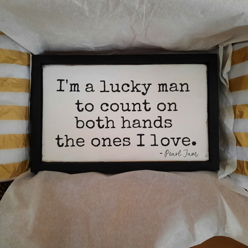May include: A black framed sign with white background and black text that reads "I'm a lucky man to count on both hands the ones I love. - Pearl Jam".
