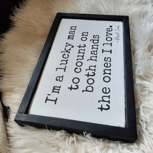 May include: A black framed wooden sign with white text that reads "I'm a lucky man to count on both hands the ones I love. - Pearl Jam".