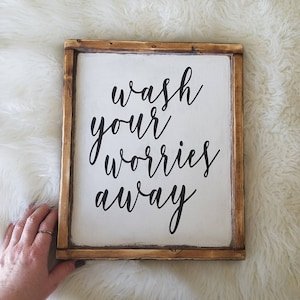 May include: A wooden sign with a white background and black lettering that reads "wash your worries away".
