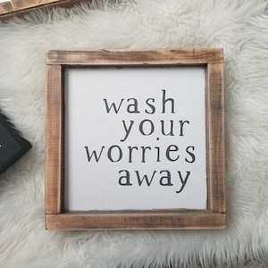 May include: A wooden framed sign with the text "wash your worries away" in black lettering on a white background.