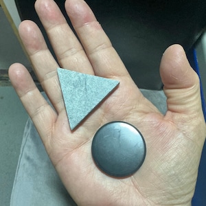 May include: A grey triangle and a black circle made of stone. The triangle is textured and the circle is smooth.