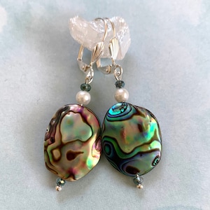 May include: A pair of iridescent abalone shell earrings with silver clip-on backs. Each earring features a white pearl and a blue crystal bead.
