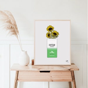 May include: A white framed print with a drawing of a bag of Counter Culture Coffee with sunflowers on top. The bag is green and has the text "Counter Culture Coffee" and "Big Trouble" on it.