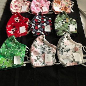 May include: Nine different fabric face masks with various patterns, including hearts, candy, dogs, plaid, shamrocks, and floral designs. Each mask is numbered 1 through 9.