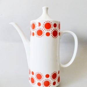 May include: White ceramic coffee pot with a red and white geometric pattern. The pot has a lid and a handle.