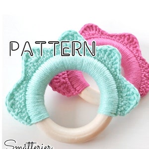 May include: Two handmade crochet baby teethers. One is light blue and the other is pink. Each teether has a wooden ring and a star-shaped crochet design. The word "PATTERN" is written in black letters on the top left.
