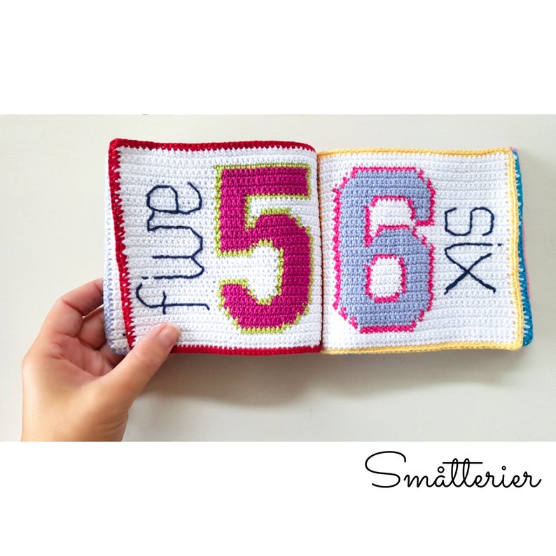 May include: A crocheted book with colorful numbers and the words "five" and "six" on the pages. The book is made of white yarn with red, yellow, and blue borders.
