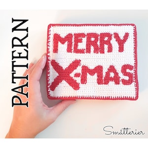 Puede incluir: Un letrero blanco tejido a crochet con letras rojas que dice "Merry Xmas".