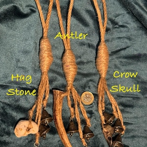 Pode incluir: Tr&ecirc;s amuletos de corda marrom com sinos. Os amuletos s&atilde;o etiquetados como "Hag Stone", "Antler" e "Crow Skull". Cada amuleto tem um objeto diferente preso &agrave; extremidade da corda. O amuleto Hag Stone tem uma pedra marrom claro presa. O amuleto Antler tem uma galhada marrom presa. O amuleto Crow Skull tem uma pequena caveira de corvo marrom presa.