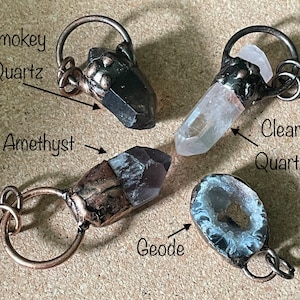 Pode incluir: Quatro pingentes de cristal com la&ccedil;os de arame de cobre. Os cristais s&atilde;o quartzo fumado, quartzo transparente, ametista e uma geoda.