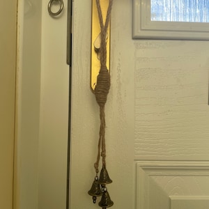 Pode incluir: Uma porta com uma ma&ccedil;aneta de porta dourada e uma corda com tr&ecirc;s pequenos sinos dourados pendurados nela.