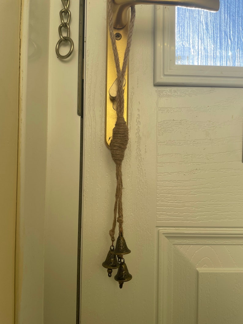 Pode incluir: Uma porta com uma ma&ccedil;aneta de porta dourada e uma corda com tr&ecirc;s pequenos sinos dourados pendurados nela.