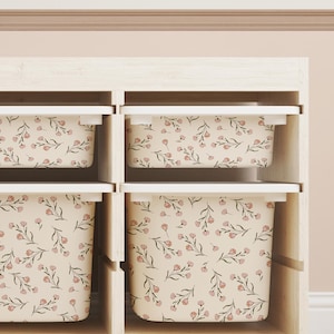 May include: A wooden storage unit with six compartments, each containing a floral-patterned bin. The bins feature a cream background with pink flowers and green stems. The unit is made of light-coloured wood.
