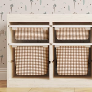 May include: A white wooden shelf unit with six brown and white checkered storage bins. The shelf unit is against a wall with a light pink and brown patterned wallpaper.