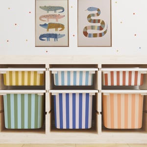 May include: A wooden storage unit with six colorful striped bins. The bins are yellow, blue, and orange, with white lids. Above are two framed art prints featuring crocodiles and a snake.